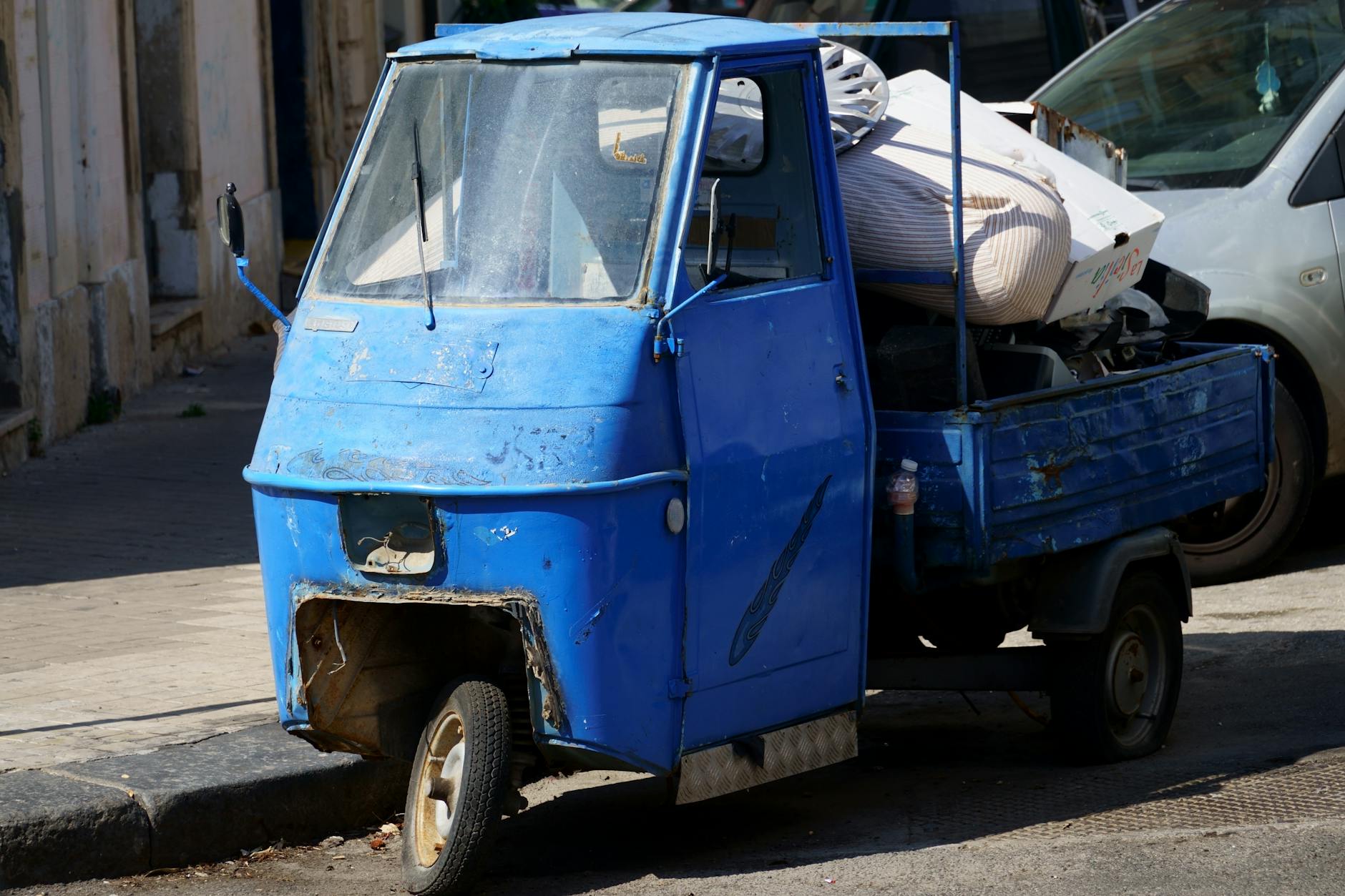 Niebieska, zniszczona trójkołowa riksza pełna gratów na miejskiej ulicy