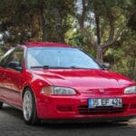 Czerwony hatchback Honda Civic zaparkowany na tle drzew