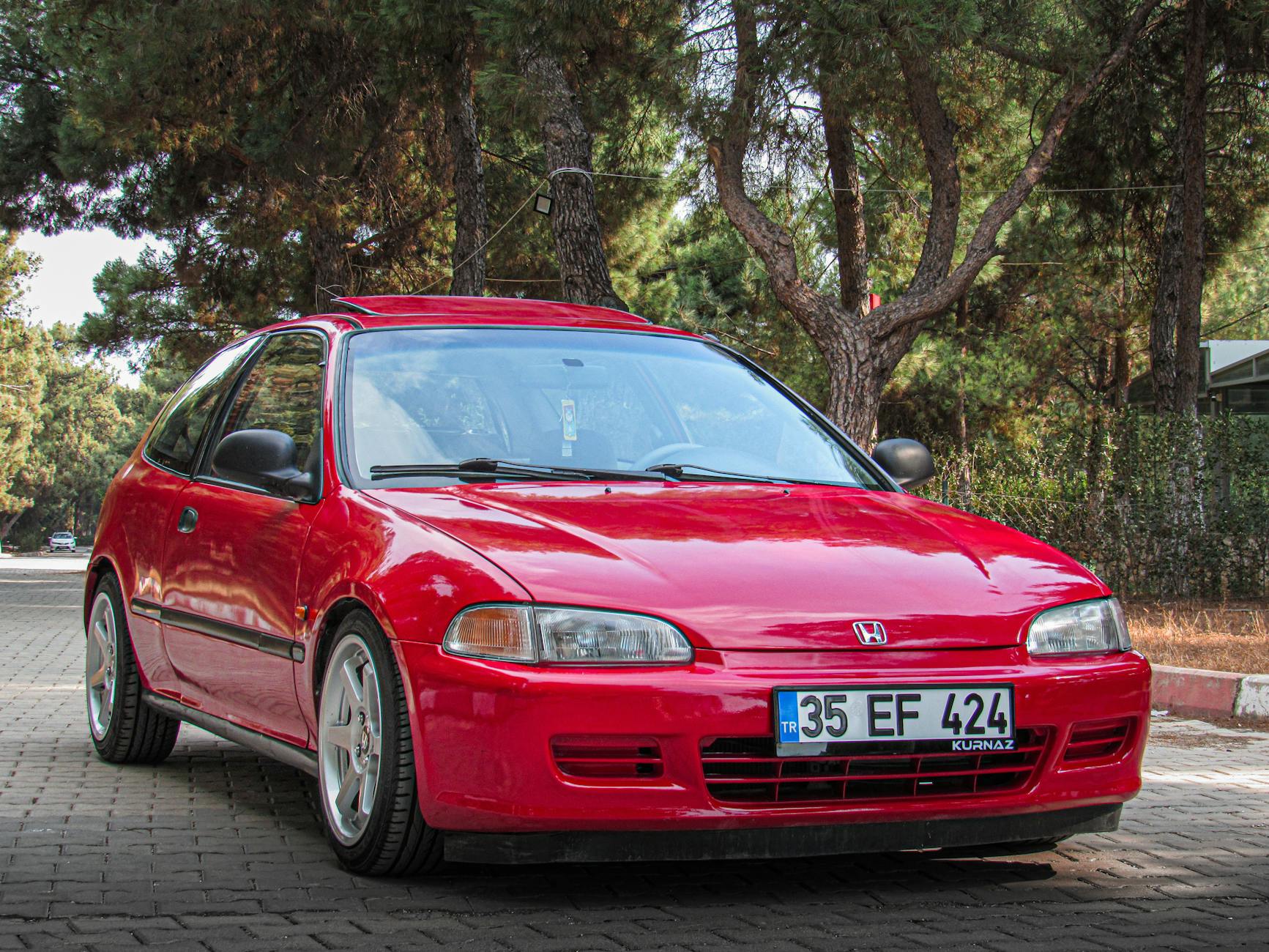 Lampy robocze i ostrzegawcze LED – kompletne oświetlenie do bezpiecznej i wydajnej pracy Czerwony hatchback Honda Civic zaparkowany na tle drzew