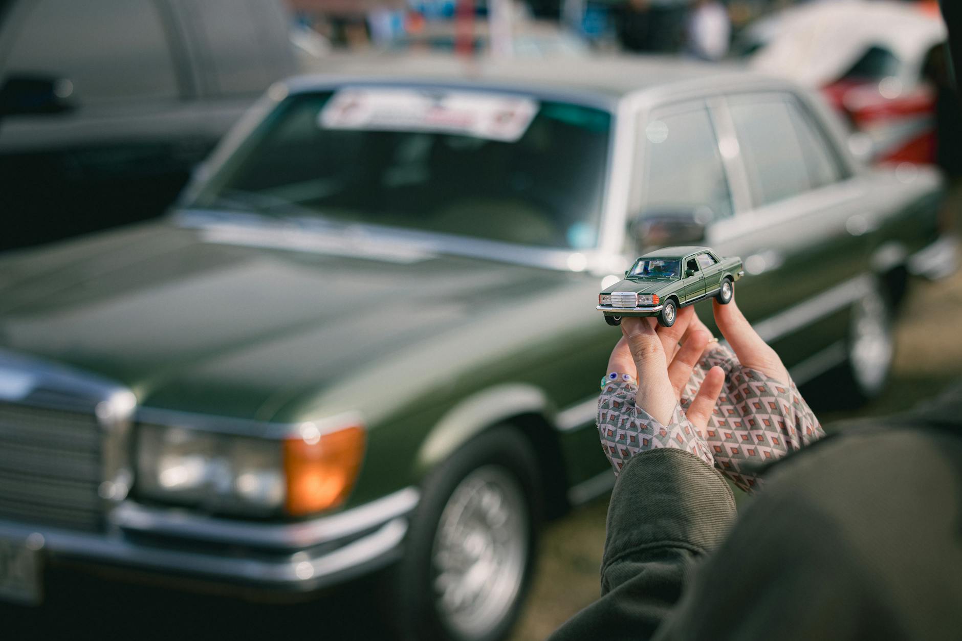 Zielony Mercedes W116 i trzymany w dłoniach miniaturowy model auta