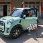 Czy Opel zaryzykuje małe auto miejskie na prąd? Kobieta wysiada z kolorowego elektrycznego auta miejskiego wśród dekoracji